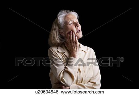 Stock Photograph - Senior woman suffering with toothache against black background. Fotosearch