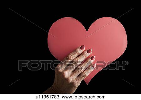 Stock Image - Senior woman's hand holding heart-shaped cardboard. Fotosearch