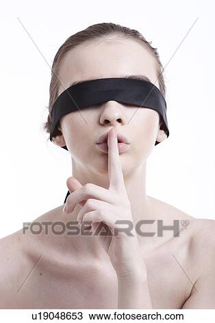 Stock Image - Shirtless young woman with blindfold gesturing to be silent against white background. Fotosearch