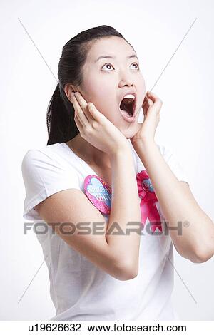 Stock Image - Shocked young Asian woman with hands on face against white background. Fotosearch