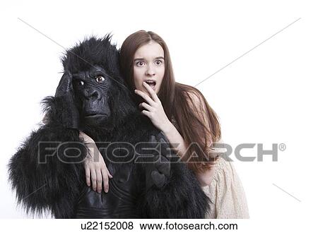 Stock Photo - Shocked young woman with irritated man in gorilla costume against white background. Fotosearch