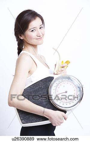 Side view of young Asian woman holding banana and weight scale against white background View Large Photo Image Stock Photo - Side view of young Asian woman holding banana and weight scale against white background. Fotosearch