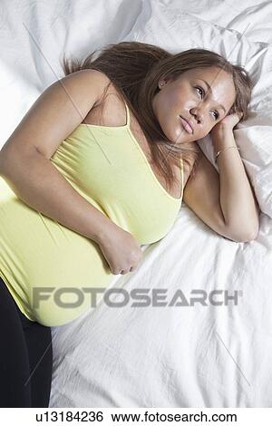 Thoughtful young pregnant woman relaxing on bed at home View Large Photo Image Stock Photograph - Thoughtful young pregnant woman relaxing on bed at home. Fotosearch