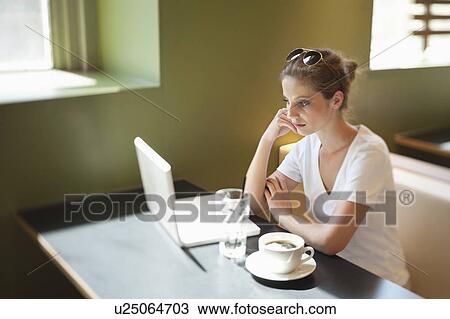 Thoughtful young woman looking at laptop while sitting at cafe View Large Photo Image Stock Image - Thoughtful young woman looking at laptop while sitting at cafe. Fotosearch