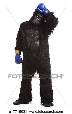 Stock Image - Tired young man in gorilla costume and boxing gloves against white background. Fotosearch