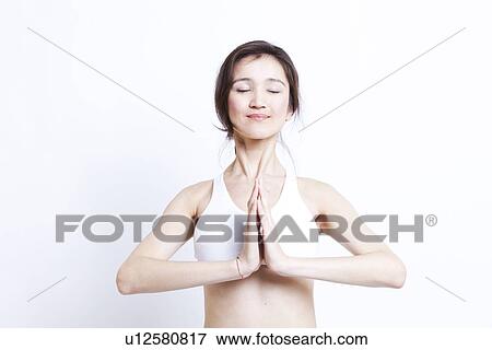 Stock Photo - Young Asian woman in white sports bra meditating against white background. Fotosearch