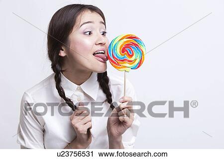 Young Asian woman licking a multicolored lollipop against white background View Large Photo Image Stock Image - Young Asian woman licking a multicolored lollipop against white background. Fotosearch
