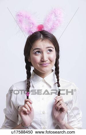 Young Asian woman with bunny ears daydreaming against white background View Large Photo Image Stock Image - Young Asian woman with bunny ears daydreaming against white background. Fotosearch