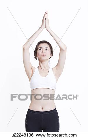 Stock Photograph - Young Asian woman with hands clasped practicing yoga against white background. Fotosearch