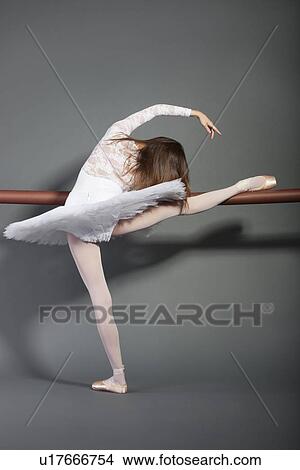Picture - Young female ballet dancer stretching at ballet bar over grey background. Fotosearch
