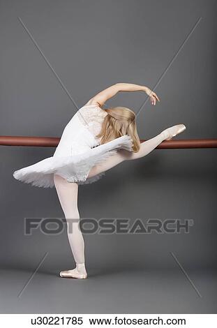 Young female ballet dancer stretching at ballet bar over grey background View Large Photo Image Stock Photography - Young female ballet dancer stretching at ballet bar over grey background. Fotosearch