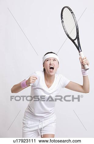 Stock Image - Young female tennis player with racket cheering against white background. Fotosearch