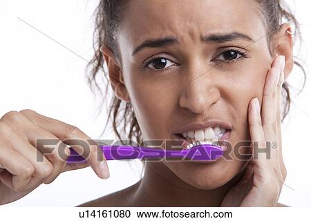 Stock Image - Young Mixed Race woman with toothbrush suffering from toothache against white background. Fotosearch