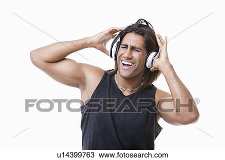Stock Image - Young muscular man listening music through headphones over white background. Fotosearch