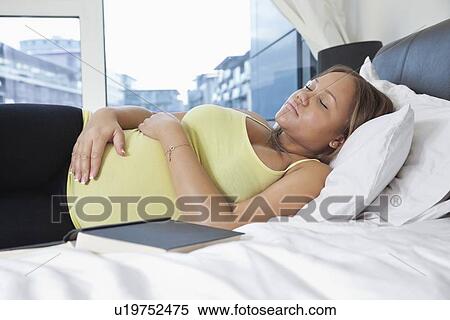Stock Photography - Young pregnant woman sleeping on bed at home. Fotosearch