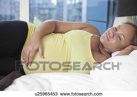 Young pregnant woman smiling while sleeping on bed at home View Large Photo Image Stock Image - Young pregnant woman smiling while sleeping on bed at home. Fotosearch