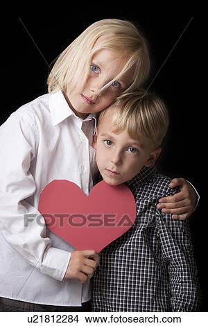 Young sister and brother hugging and holding a red cardboard heart looking sad at the camera View Large Photo Image Picture - Young sister and brother hugging and holding a red cardboard heart looking sad at the camera. Fotosearch