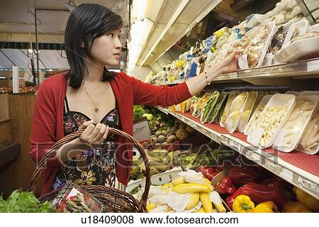 Stock Photo - Young woman choosing mushroom package in market. Fotosearch