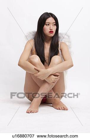 Stock Photo - Young woman with angel wings sitting on floor against white background. Fotosearch