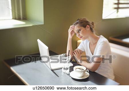 Stock Image - Young woman working on laptop at cafe. Fotosearch