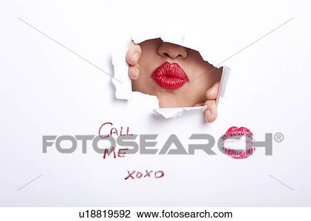 Stock Image - Young woman's red puckered lips seen through ripped paper with text and lipstick mark. Fotosearch