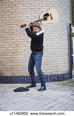Aggressive young man breaking guitar against brick wall on street View Large Photo Image Stock Image - Aggressive young man breaking guitar against brick wall on street. Fotosearch