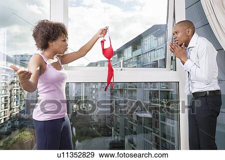 Stock Photo - Angry young woman holding bra in front of guilty man at home. Fotosearch