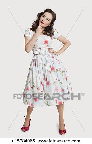 Stock Photography - Beautiful young woman in dress day dreaming with hand on chin against white background. Fotosearch