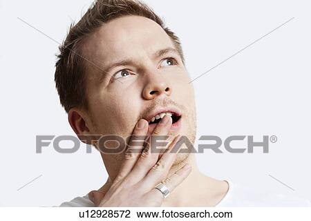 Contemplative young man with hand over mouth against white background View Large Photo Image Stock Image - Contemplative young man with hand over mouth against white background. Fotosearch