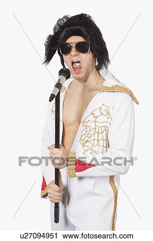 Elvis impersonator singing into a microphone against gray background View Large Photo Image Stock Image - Elvis impersonator singing into a microphone against gray background. Fotosearch