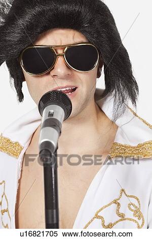 Elvis impersonator singing into a microphone against gray background View Large Photo Image Stock Photography - Elvis impersonator singing into a microphone against gray background. Fotosearch
