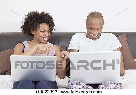 Stock Photo - Excited young African American couple using laptops on bed. Fotosearch
