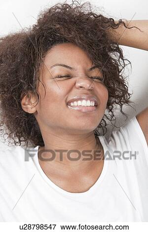 Stock Photo - Excited young African American woman with hands in hair smiling against white background. Fotosearch