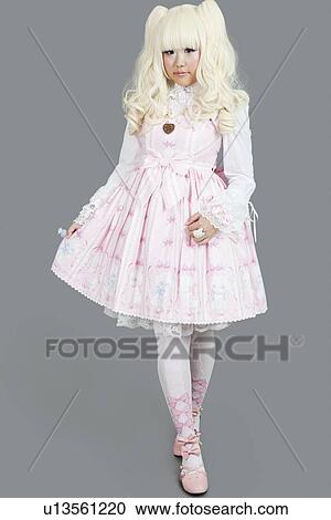 Stock Image - Full length of young woman dressed as a doll over gray background. Fotosearch