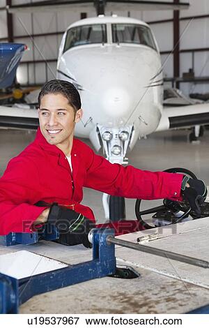 Happy aviation mechanic driving cart in airplane hangar View Large Photo Image Stock Photo - Happy aviation mechanic driving cart in airplane hangar. Fotosearch