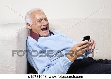 Stock Photo - Happy elderly man using cell phone at home. Fotosearch