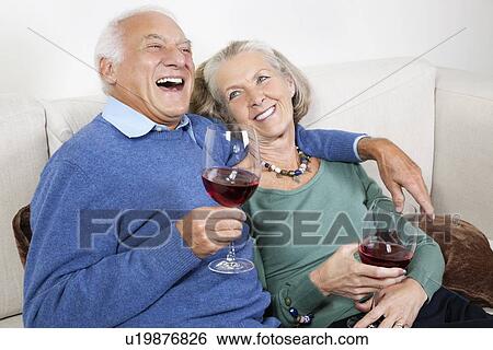Happy senior couple with red wine glasses while sitting on sofa at home View Large Photo Image Stock Photograph - Happy senior couple with red wine glasses while sitting on sofa at home. Fotosearch