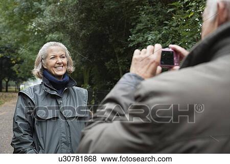 Happy senior woman being photographed by husband at park View Large Photo Image Stock Photo - Happy senior woman being photographed by husband at park. Fotosearch