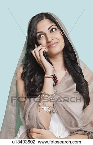 Happy thoughtful young Asian woman in traditional clothing using cell phone against blue background View Large Photo Image Stock Image - Happy thoughtful young Asian woman in traditional clothing using cell phone against blue background. Fotosearch