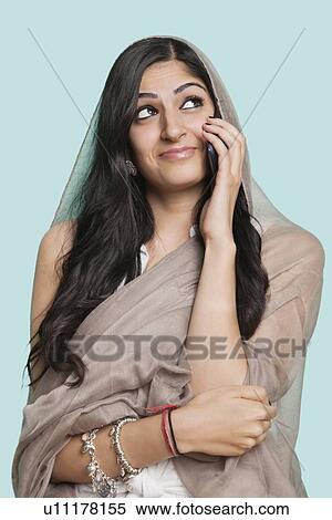 Happy thoughtful young Muslim woman in traditional clothing using cell phone against blue background View Large Photo Image Stock Photography - Happy thoughtful young Muslim woman in traditional clothing using cell phone against blue background. Fotosearch