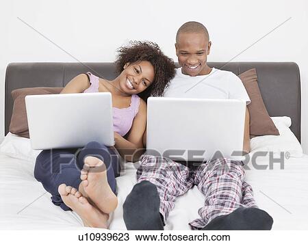 Happy young African American couple using laptops on bed View Large Photo Image Stock Image - Happy young African American couple using laptops on bed. Fotosearch