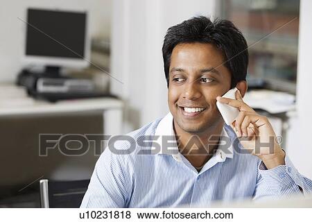 Happy young businessman using cell phone at office View Large Photo Image Stock Photo - Happy young businessman using cell phone at office. Fotosearch
