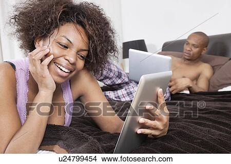 Happy young woman using tablet PC with man in background View Large Photo Image Picture - Happy young woman using tablet PC with man in background. Fotosearch