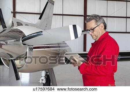 Picture - Mature aviation mechanic using tablet PC in front of airplane. Fotosearch