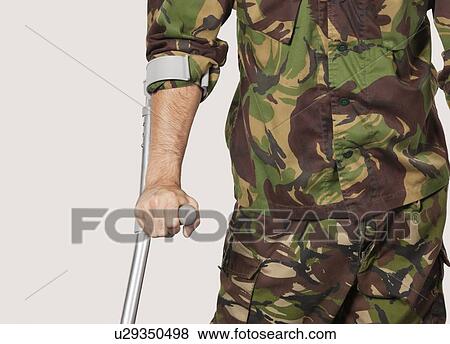 Mid section of young soldier holding crutches against gray background View Large Photo Image Stock Photo - Mid section of young soldier holding crutches against gray background. Fotosearch