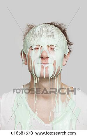 Stock Image - Paint dripping down a young Caucasian man's face against gray background. Fotosearch