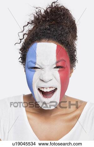Picture - Portrait of angry young African American woman with French flag painted on face shouting against white background. Fotosearch