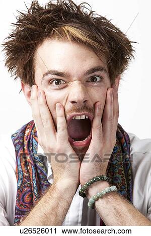 Stock Image - Portrait of angry young man screaming against white background. Fotosearch