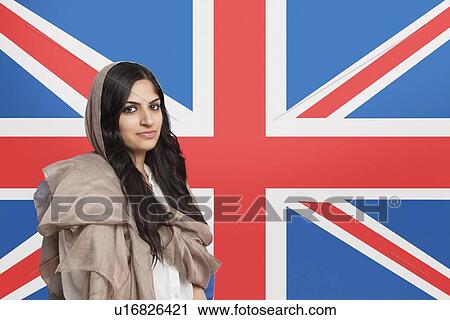 Stock Image - Portrait of beautiful young Muslim woman in traditional clothing standing against British flag. Fotosearch