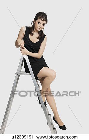 Portrait of beautiful young woman in dress sitting on step ladder against white background View Large Photo Image Stock Image - Portrait of beautiful young woman in dress sitting on step ladder against white background. Fotosearch